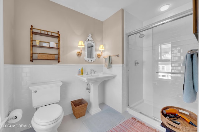 bathroom featuring toilet, wainscoting, a stall shower, tile patterned floors, and tile walls