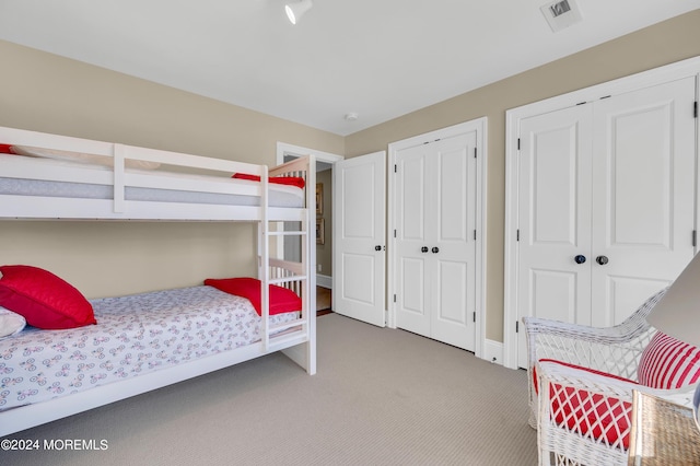 bedroom with visible vents, light carpet, two closets, and baseboards