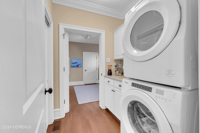 clothes washing area with wood finished floors, visible vents, cabinet space, ornamental molding, and stacked washer / dryer