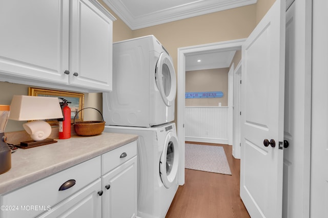 laundry room featuring a wainscoted wall, ornamental molding, stacked washer and clothes dryer, wood finished floors, and cabinet space