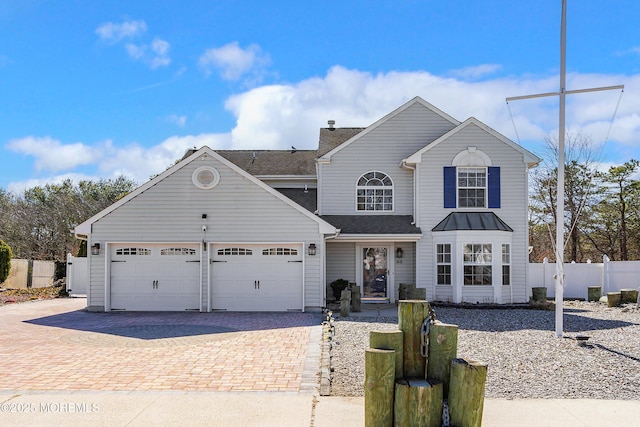 traditional-style house with decorative driveway, fence, a garage, and roof with shingles