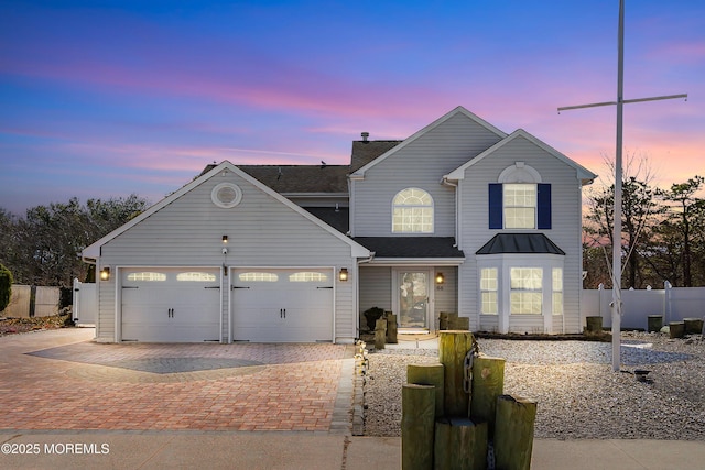 traditional-style house with an attached garage, decorative driveway, and fence