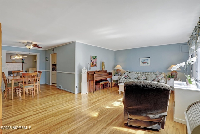 living area with a fireplace, baseboards, light wood-type flooring, and ceiling fan