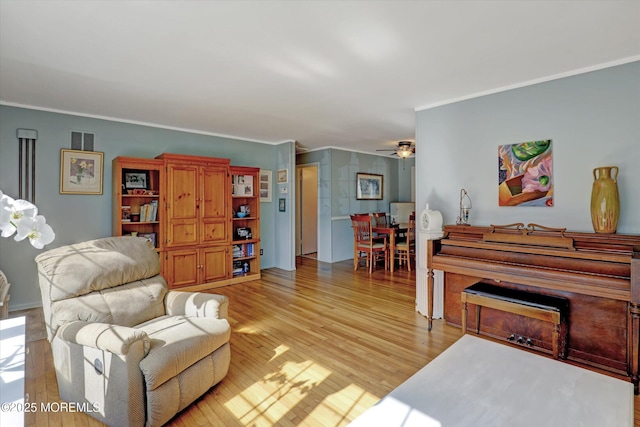 living area featuring crown molding, light wood-style flooring, visible vents, and ceiling fan