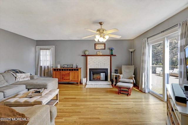 living room featuring a brick fireplace, light wood finished floors, and ceiling fan