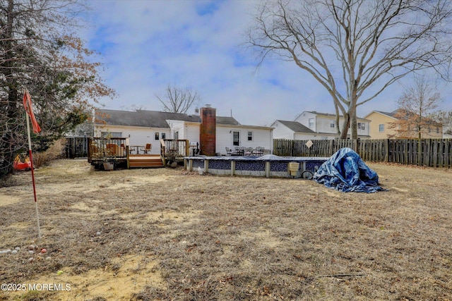 rear view of house featuring a deck, a fenced backyard, and a chimney