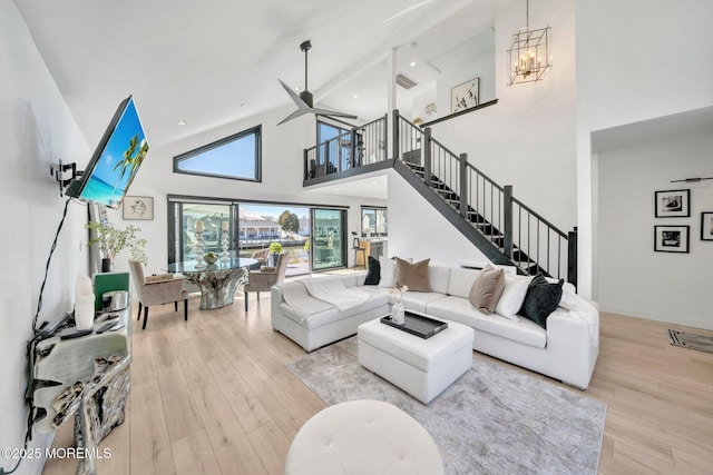 living room with stairs, ceiling fan with notable chandelier, wood finished floors, and high vaulted ceiling