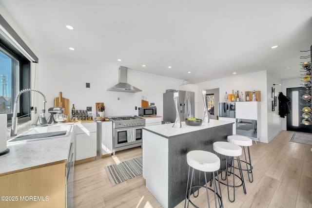 kitchen featuring wall chimney exhaust hood, light wood-style floors, appliances with stainless steel finishes, and a sink