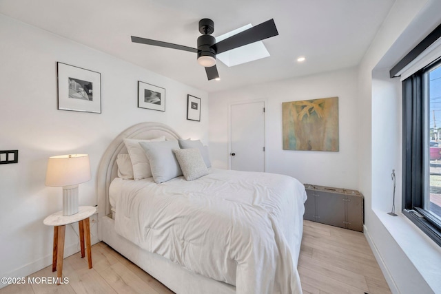 bedroom with a ceiling fan, a skylight, baseboards, and light wood-type flooring