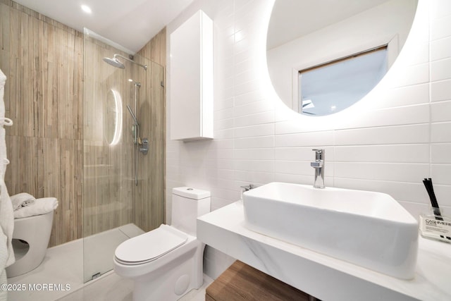 bathroom featuring a tile shower, a sink, tile walls, toilet, and backsplash