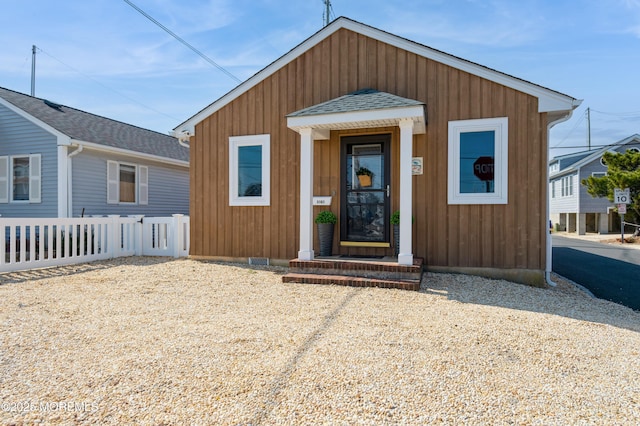 view of front facade with fence, roof with shingles, and crawl space