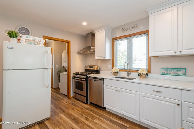 kitchen featuring light wood-style flooring, a sink, appliances with stainless steel finishes, wall chimney exhaust hood, and white cabinets