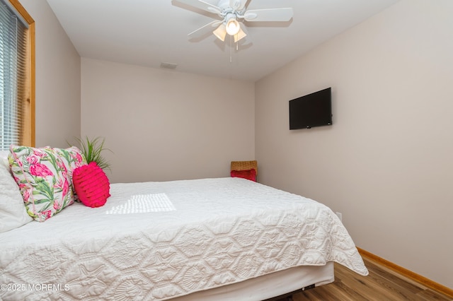 bedroom with a ceiling fan, visible vents, wood finished floors, and baseboards