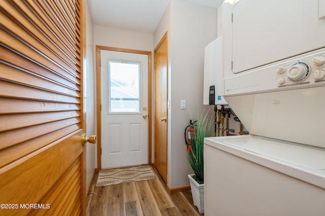 doorway to outside featuring light wood-style floors, baseboards, stacked washer and dryer, and water heater