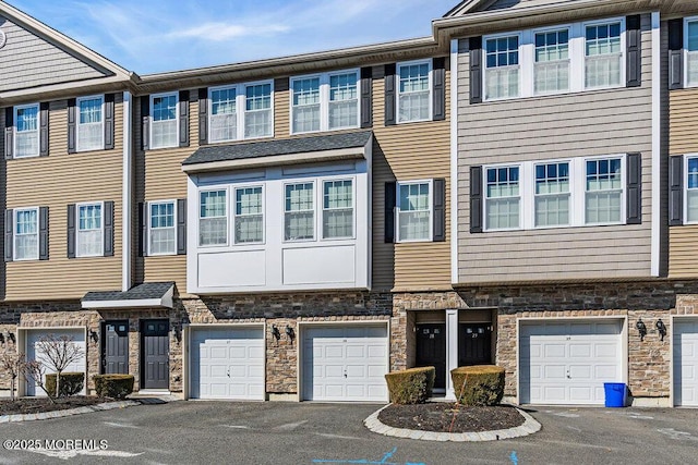 multi unit property featuring stone siding, driveway, and a garage