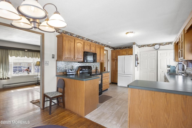 kitchen with dark countertops, a baseboard radiator, a peninsula, black appliances, and a sink