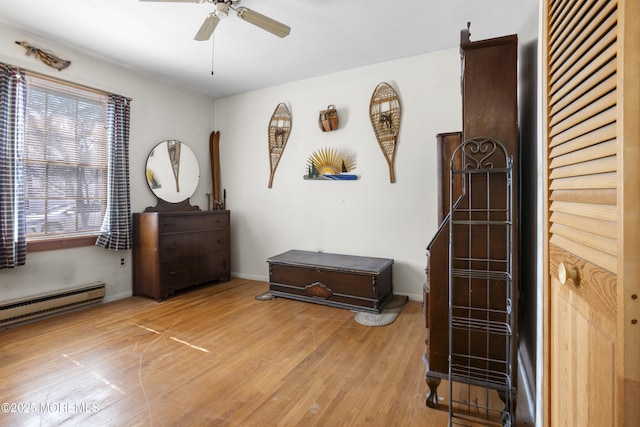 interior space featuring a baseboard heating unit, baseboards, light wood finished floors, and ceiling fan