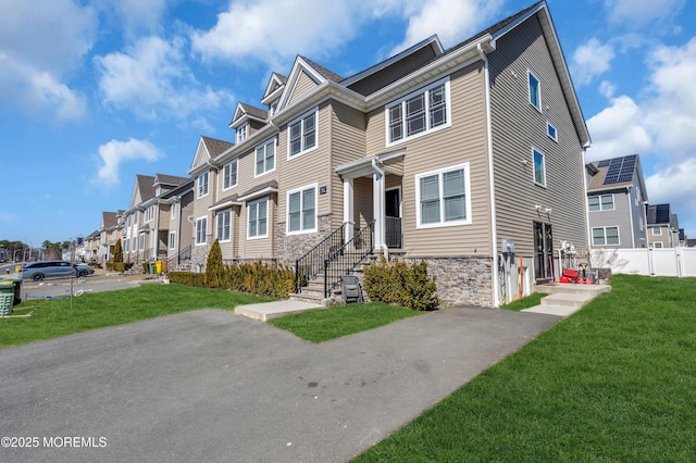 multi unit property with a residential view, stone siding, a front lawn, and fence