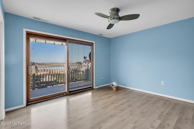 unfurnished room with wood finished floors, a healthy amount of sunlight, visible vents, and baseboards