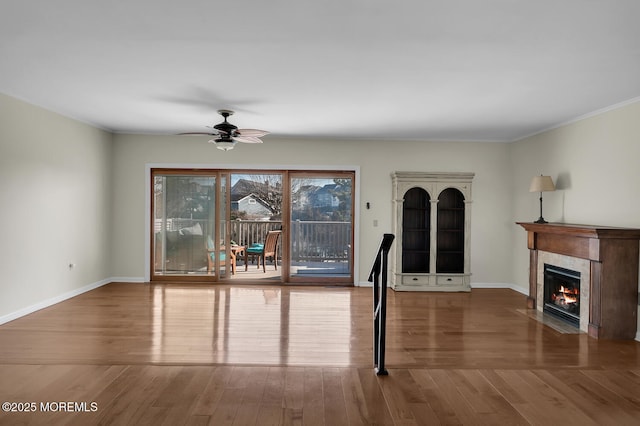 unfurnished dining area featuring a fireplace, baseboards, ceiling fan, and wood finished floors