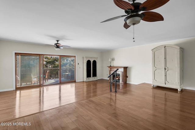 unfurnished living room featuring a lit fireplace, baseboards, ceiling fan, and wood finished floors