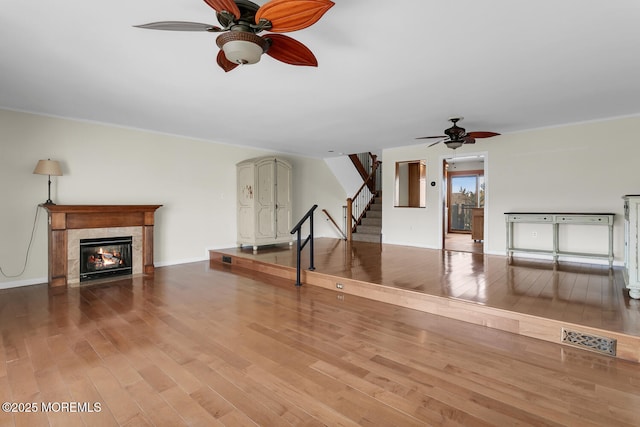 unfurnished living room with stairs, a fireplace with flush hearth, wood finished floors, and ceiling fan