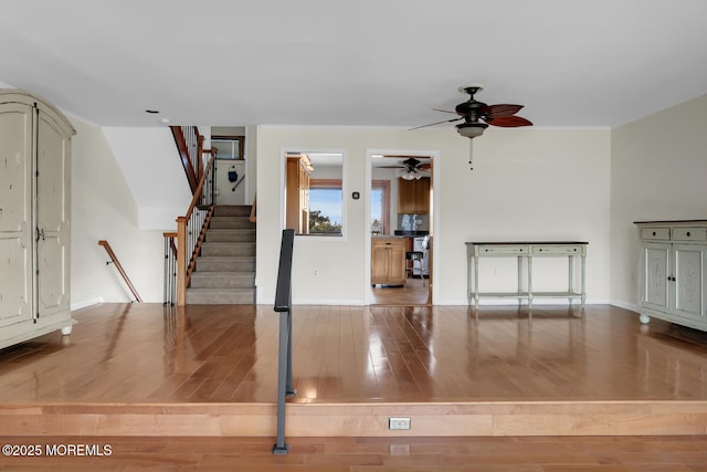 unfurnished living room with crown molding, baseboards, stairway, wood finished floors, and a ceiling fan