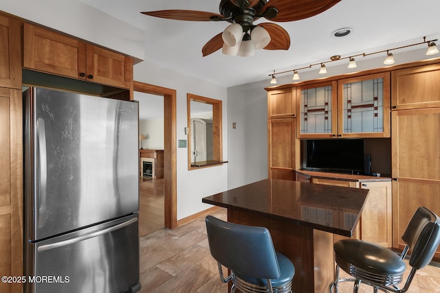 kitchen with brown cabinetry, a kitchen breakfast bar, a ceiling fan, and freestanding refrigerator