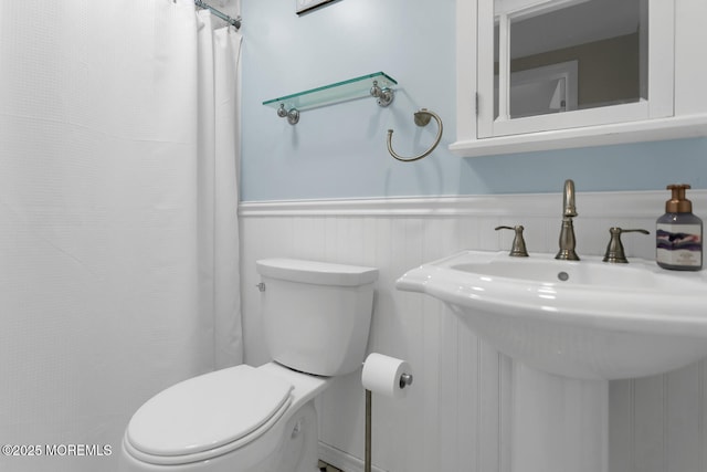 bathroom with a shower with curtain, toilet, a wainscoted wall, and a sink