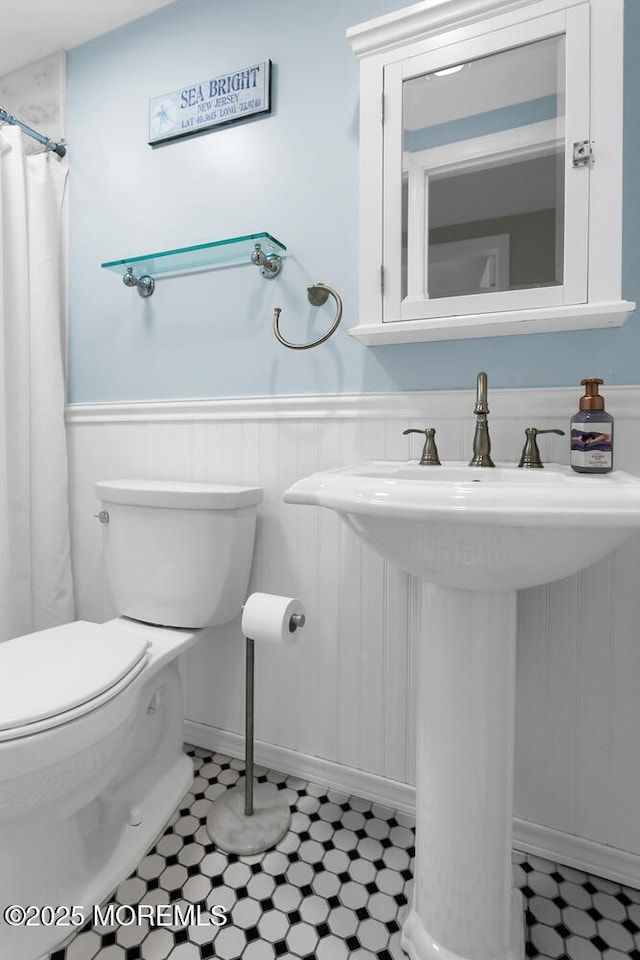 full bath with tile patterned floors, a wainscoted wall, toilet, and a sink