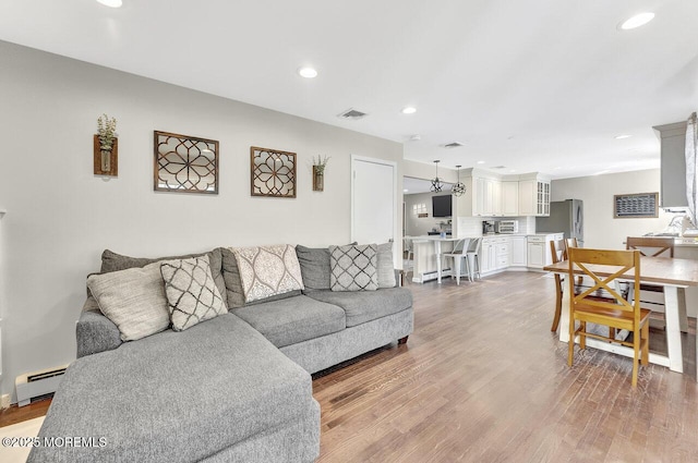 living room with a baseboard heating unit, recessed lighting, visible vents, and light wood-type flooring