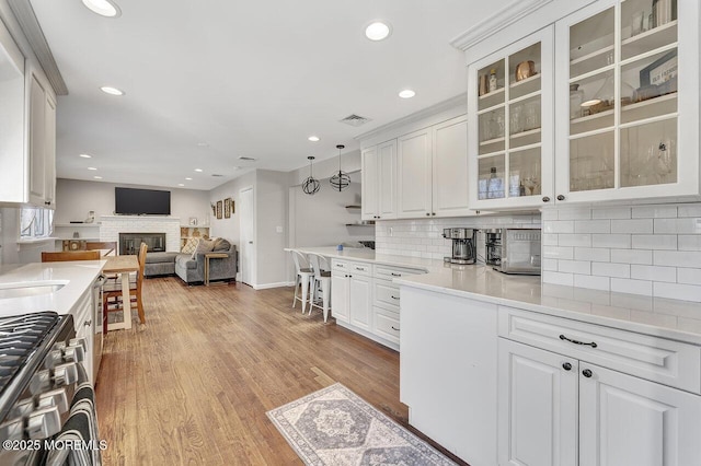 kitchen with stainless steel gas range oven, visible vents, open floor plan, light wood-type flooring, and white cabinets