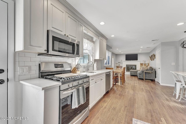 kitchen with light countertops, light wood-style flooring, appliances with stainless steel finishes, a glass covered fireplace, and a sink