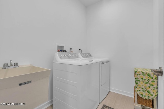 washroom featuring a sink, separate washer and dryer, light wood finished floors, baseboards, and laundry area
