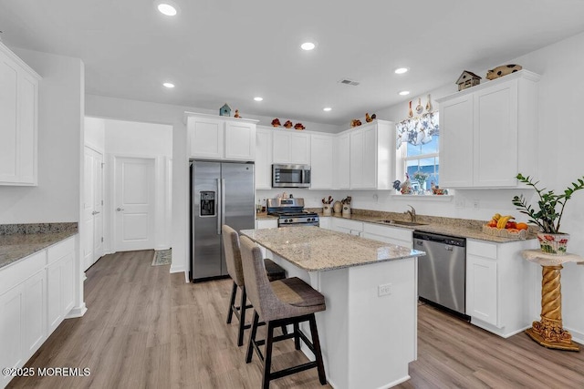 kitchen featuring a kitchen bar, light wood-style flooring, a center island, appliances with stainless steel finishes, and white cabinets