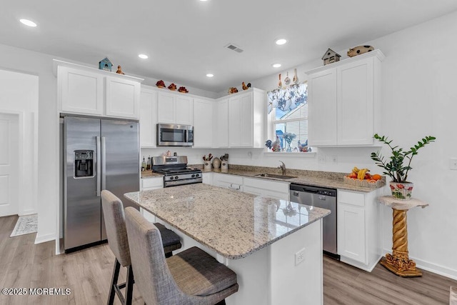 kitchen with a sink, a kitchen island, stainless steel appliances, white cabinets, and light stone countertops