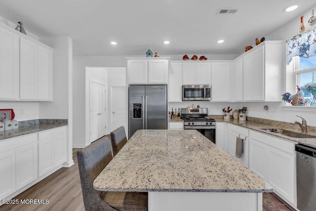kitchen featuring wood finished floors, recessed lighting, a sink, white cabinets, and appliances with stainless steel finishes