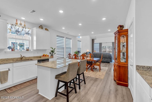 kitchen featuring a kitchen breakfast bar, light wood-style flooring, visible vents, and a sink