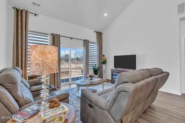 living area with visible vents, baseboards, high vaulted ceiling, and wood finished floors