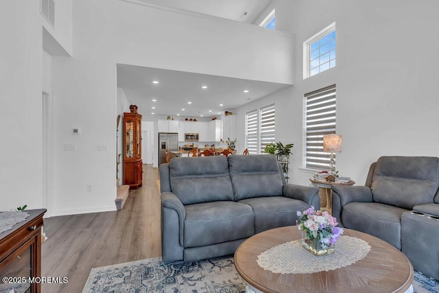 living room with visible vents, baseboards, light wood-style flooring, recessed lighting, and a towering ceiling