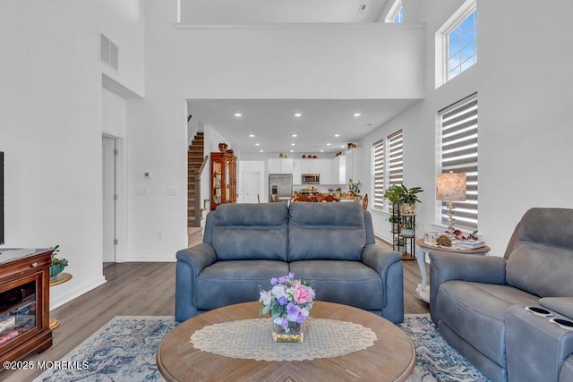 living area featuring visible vents, baseboards, stairs, a towering ceiling, and light wood-type flooring