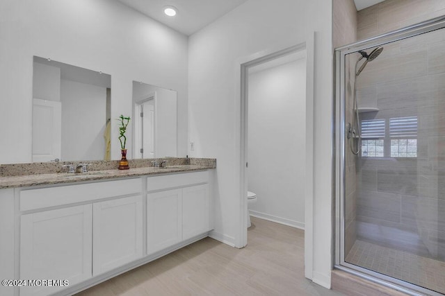 full bath featuring baseboards, toilet, double vanity, a stall shower, and a sink