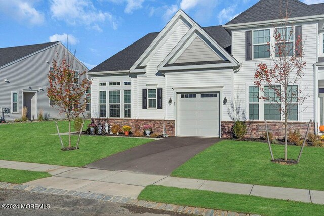 view of front of house featuring a front yard, driveway, a shingled roof, stone siding, and a garage