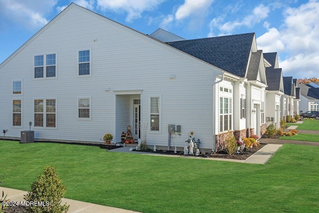 rear view of house with cooling unit, a lawn, and a shingled roof