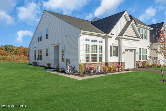 view of front of house featuring a front yard, roof with shingles, central AC unit, stone siding, and an attached garage