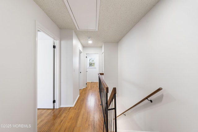 corridor with baseboards, attic access, a textured ceiling, an upstairs landing, and light wood-type flooring