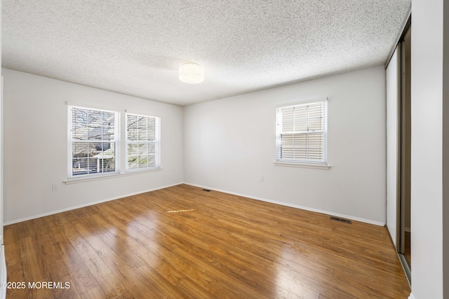 unfurnished bedroom featuring visible vents, hardwood / wood-style flooring, a textured ceiling, a closet, and baseboards