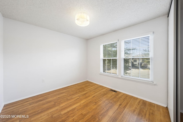 empty room with baseboards, wood finished floors, visible vents, and a textured ceiling