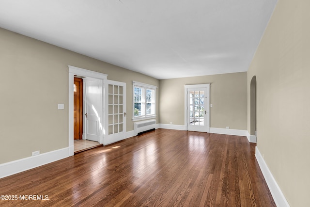 interior space featuring radiator heating unit, wood finished floors, arched walkways, and baseboards