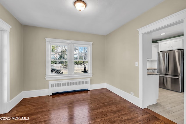 unfurnished room featuring baseboards, radiator, and wood finished floors